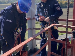 Policjanci podczas szkolenia z ratownikami CSRG. Policjanci wiążący linę. w tle pola i droga.