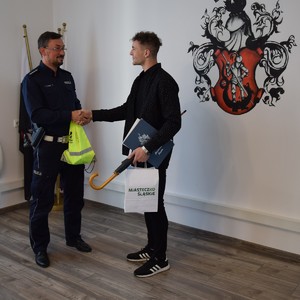 zastępca naczelnika WRD gratulujący panu Łukaszowi i przekazujący upominki w odblaskowej torbie.