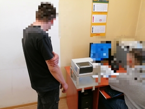 mężczyzna z zamazaną twarzą stojący obok policjanta pracującego na komputerze