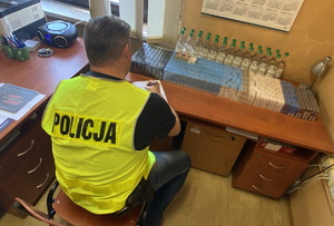 policjant przy biurku na którym leżą papierosy i butelki z alkoholem