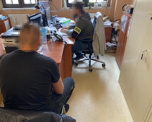 policjant z opaską na ramieniu z napisem policja w trakcie czynności z zatrzymanym w pomieszczeniu komendy