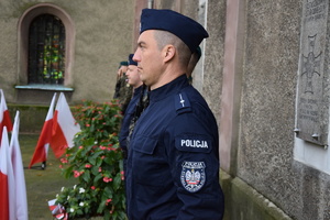 na pierwszym planie policjant pełniący wartę honorową pod pamiątkową tablicą