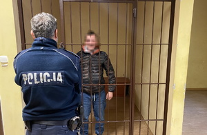policjant w pomieszczeniu komendy, za kratami stoi osoba zatrzymana