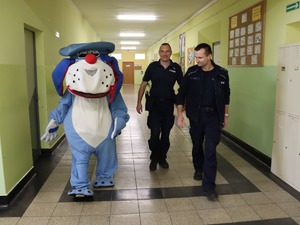 na zdjęciu policyjna maskotka sznupek wędrująca korytarzem w towarzystwie policjantów