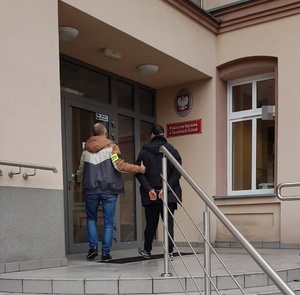 Na zdjęciu policjant wraz z zatrzymanym mężczyzną przed budynkiem Prokuratury.