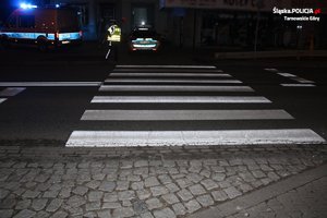 na zdjęciu po zmroku przejście dla pieszych, przy którym stoją dwa radiowozy i policjant