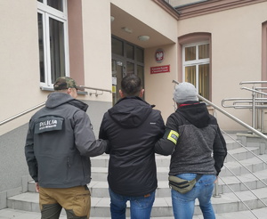 na zdjęciu policjanci w ubiorze cywilnym prowadzą zatrzymanego do budynku prokuratury