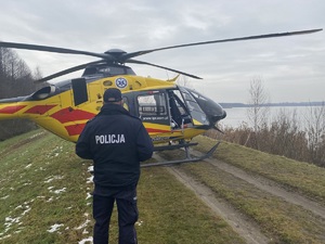 na zdjęciu policjant przy śmigłowcu lotniczego pogotowia ratunkowego, który stoi przy zbiorniku wodnym