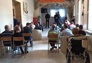 na zdjęciu pensjonariusze słuchają prelekcji policjantów, którzy stoją naprzeciwko nich