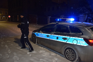 na zdjęciu policyjny radiowóz zaparkowany na zaśnieżonej drodze, obok policjant