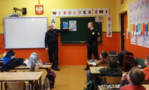 na zdjęciu policjant i strażnicy miejscy w sali szkolnej, w trakcie spotkania z uczniami