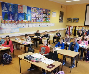 na zdjęciu dzieci w szkolnych ławkach, w trakcie spotkania z policjantem i strażnikami miejskimi