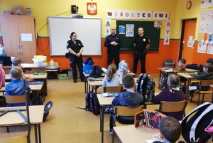 na zdjęciu policjant i strażnicy miejscy w sali szkolnej, w trakcie spotkania z uczniami