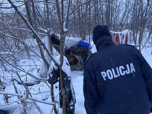 na zdjęciu policjant w trakcie sprawdzania zaśnieżonego miejsca, gdzie mogą przebywać osoby bezdomne