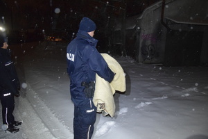 na zdjęciu policjant trzymający w ręku koc, w trakcie akcji &quot;bezdomni&quot;