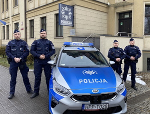 na zdjęciu policjanci przy radiowozie przed budynkiem komendy