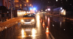 na zdjęciu miejsce wypadku drogowego. Na jezdni samochód osobowy, a za nim policyjny radiowóz. Na środku drogi policjant.