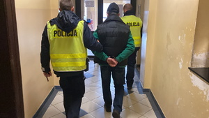 na zdjęciu policjanci prowadzą zatrzymanego korytarzem komendy