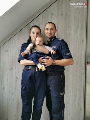 na zdjęciu policjanci w mundurach, którzy na rękach trzymają swoje dziecko