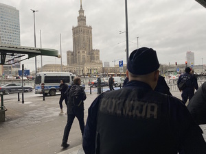 na zdjęciu policjant przemieszczający się chodnikiem, w tle widać pałac kultury i nauki w warszawie