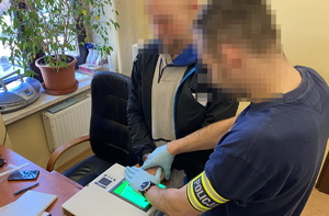 na zdjęciu technik kryminalistyki w trakcie pobierania odcisków palców od zatrzymanego