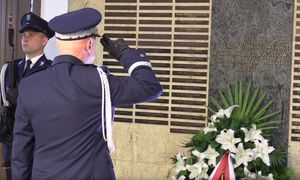 na zdjęciu policjant w mundurze galowym salutuje przed pamiątkową tablicą, pod którą są kwiaty