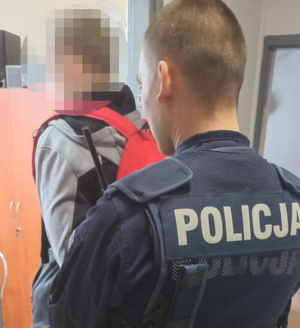 na zdjęciu policjant, który prowadzi przed sobą zatrzymanego mężczyznę