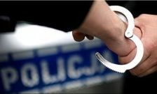 na zdjęciu ręka osoby w trakcie zakuwania w kajdanki, z tyłu napis policja na niebieskim tle