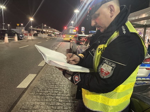 na zdjęciu policjant trzymający w ręku notatnik, stojący na ulicy