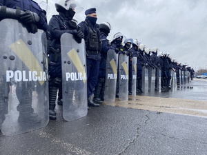 na zdjęciu policjanci w stojący w szeregu, części z nich trzyma przed sobą przezroczyste tarcze z napisem policja