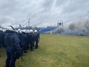 na zdjęciu pododdział policji, a przed nim stadionowy sektor, na którym doszło do zamieszek, widać czarny dym