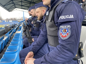 na zdjęciu widoczna naszywka na niebieskim mundurze z napisem Policja Zespół Patrolowo - Interwencyjny KMP (Komendy Miejskiej Policji) Chorzów, w tle siedzący policjanci