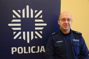 na zdjęciu dzielnicowy Golicz przy niebieskim banerze z napisem policja