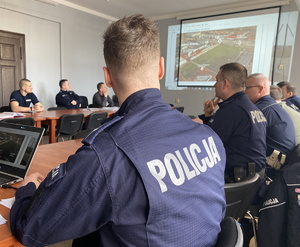 na zdjęciu policjanci w pomieszczeniu komendy, gdzie na ekranie wyświetlona jest fotografia stadionu