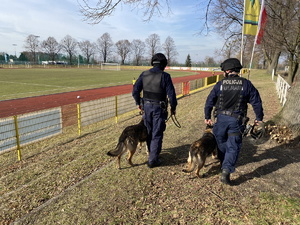 na zdjęciu dwóch policjantów z psami w trakcie patrolu na terenie stadionu