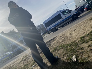 na zdjęciu policjant tyłem na trawniku, przed nim policyjne radiowozy