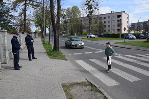 na zdjęciu policjanci przy przejściu dla pieszych, przez które idzie dziecko, w tle samochody i zabudowania
