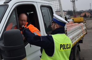na zdjęciu policjant bada trzeźwość kierującego, który siedzi w białym dostawczym aucie z paką, na sobie ma odblaskową kurtkę koloru pomarańczowego