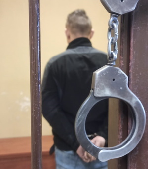 na zdjęciu kajdanki wiszące na kracie celi, w której stoi zatrzymany