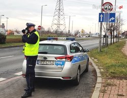 na zdjęciu policjant przy radiowozie na drodze mierzy prędkość