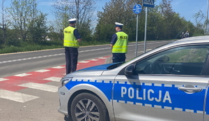 na zdjęciu radiowóz, za którym stoją policjanci przy jezdni i drodze rowerowej