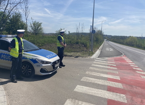 na zdjęciu policjanci przy radiowozie, przy jezdni i drodze rowerowej