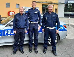 na zdjęciu od lewej Pierwszy Zastępca Komendanta Powiatowego Policji w Tarnowskich Górach nadkomisarz Waldemar Czapla, sierżant sztabowy Wojciech Feliks, młodszy aspirant Tomasz Żmuda, za nimi policyjny radiowóz i budynek