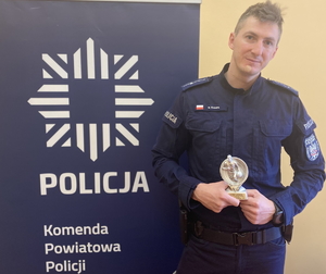 na zdjęciu dzielnicowy ze statuetką dla najlepszego zawodnika przy niebieskim banerze z napisem policja