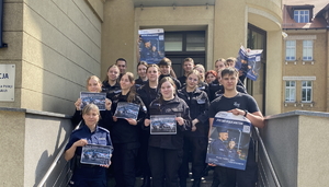 na zdjęciu uczniowie klasy mundurowej oraz policjantka na schodach komendy, część uczniów trzyma w ręce plakaty promujące zawód policjanta