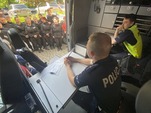 na zdjęciu policjanci w radiowozie w trakcie spotkania, przed radiowozem uczniowie