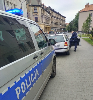 na zdjęciu policyjny radiowóz zaparkowany za białym samochodem osobowym na ulicy