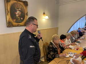 na zdjęciu policjantka i policjant w trakcie debaty z seniorami, którzy siedzą przy stole