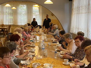na zdjęciu policjantka i policjant w trakcie debaty z seniorami, którzy siedzą przy stole