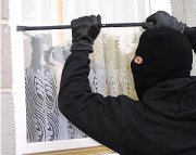 na zdjęciu zamaskowana postać z łomem w ręku wyważa drzwi